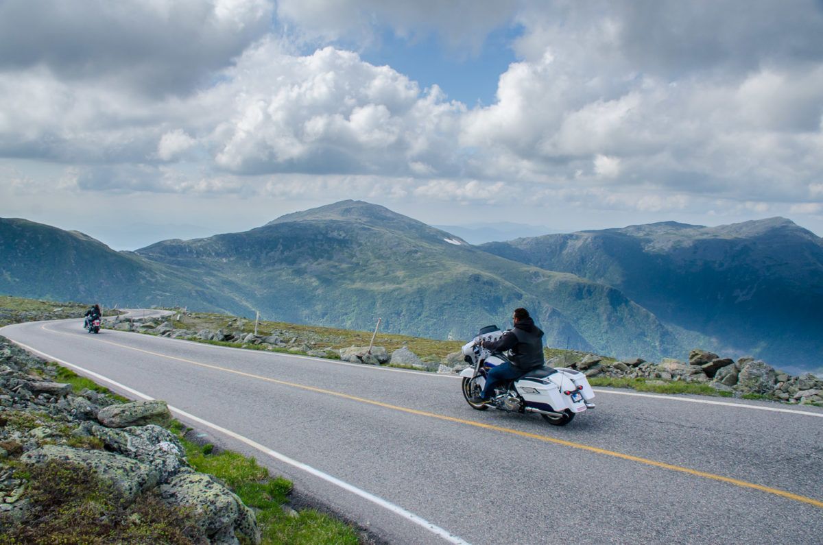 Two people are riding motorcycles down a mountain road.