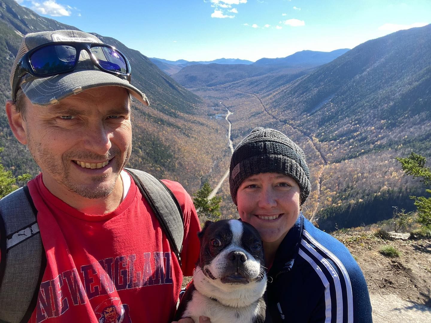 A man and a woman are holding a dog on top of a mountain.
