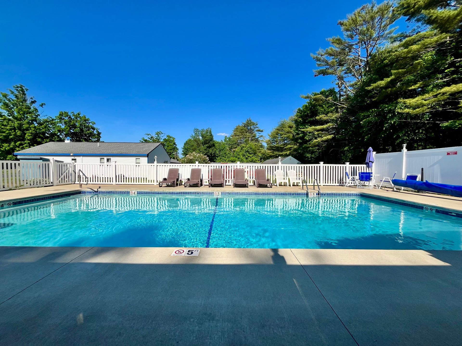 A large swimming pool with a white fence and chairs around it