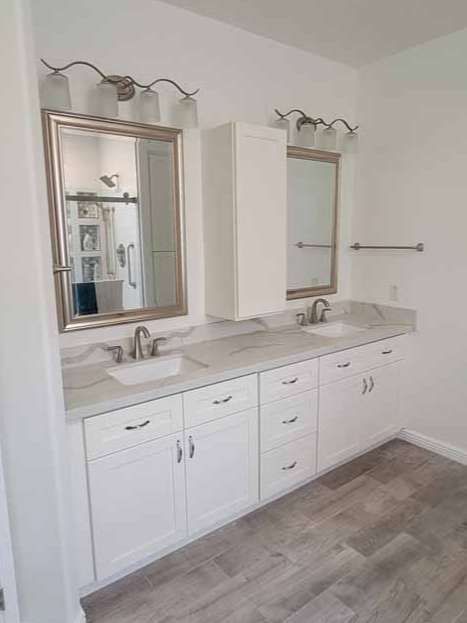 A bathroom with two sinks , a mirror , and white cabinets.