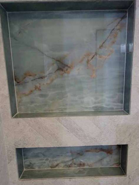 There are two shelves in the wall with marble tiles.