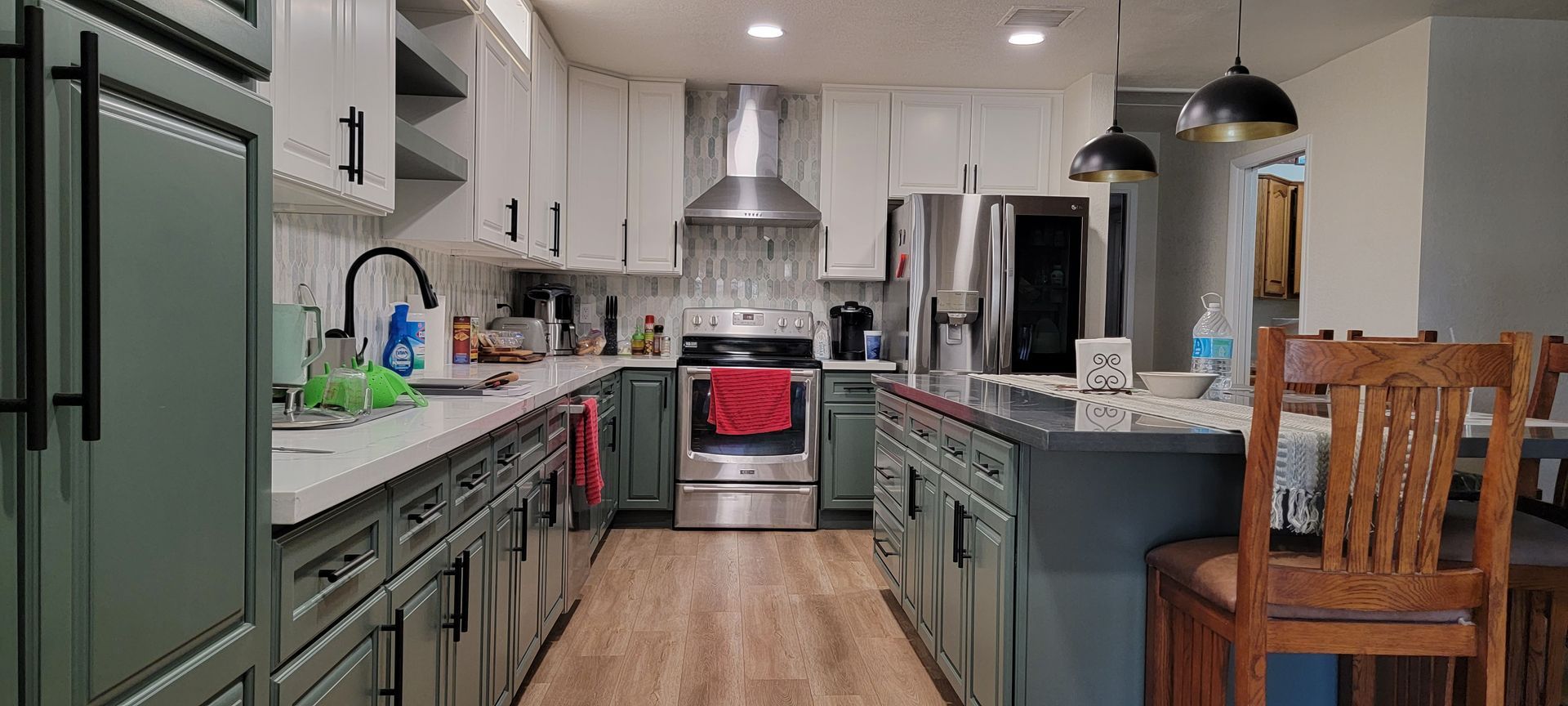 A kitchen with green cabinets , white cabinets , stainless steel appliances and a large island.