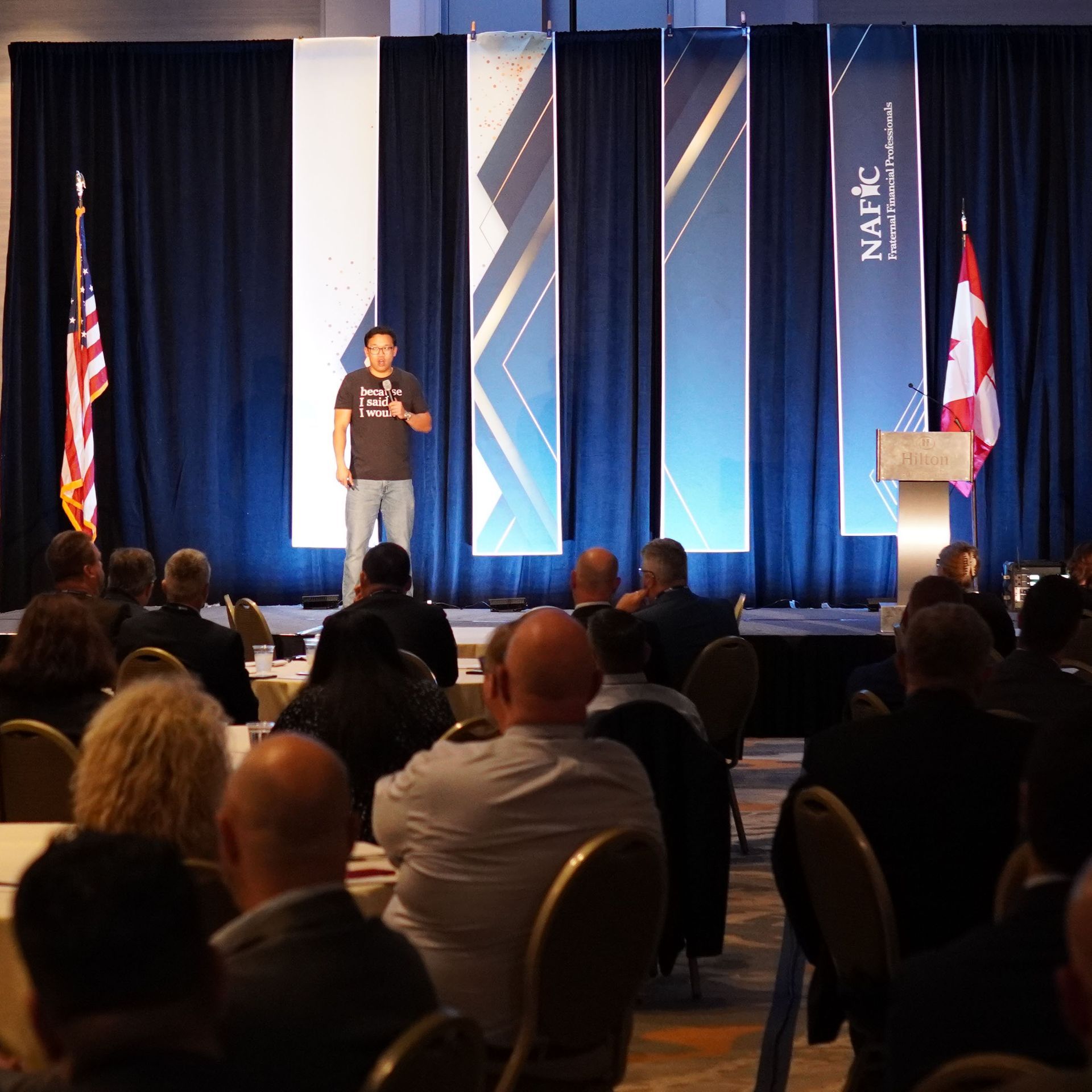 A man stands on a stage in front of a crowd with a sign that says mail inc.