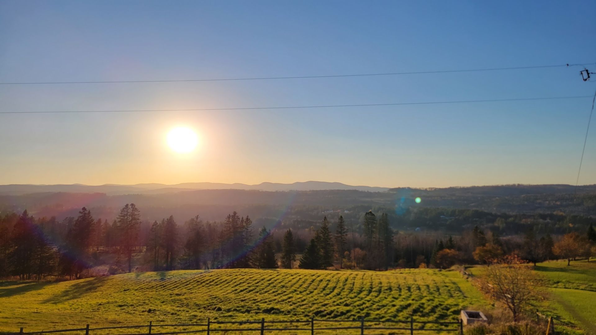 The sun is setting over a field with a fence in the foreground.