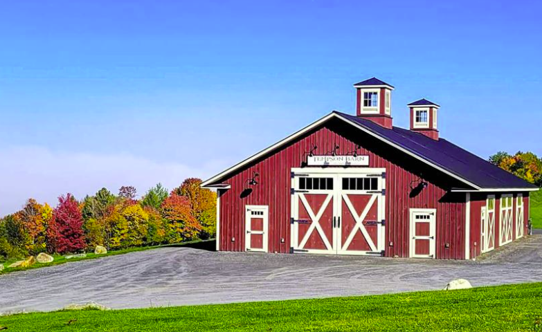 A large red barn is sitting in the middle of a grassy field.