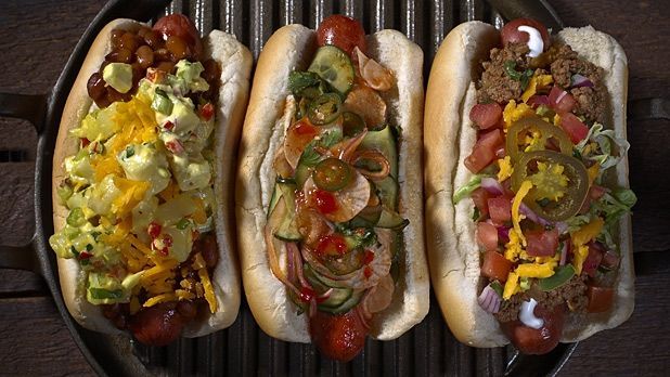 Three hot dogs with different toppings are sitting on a grill.