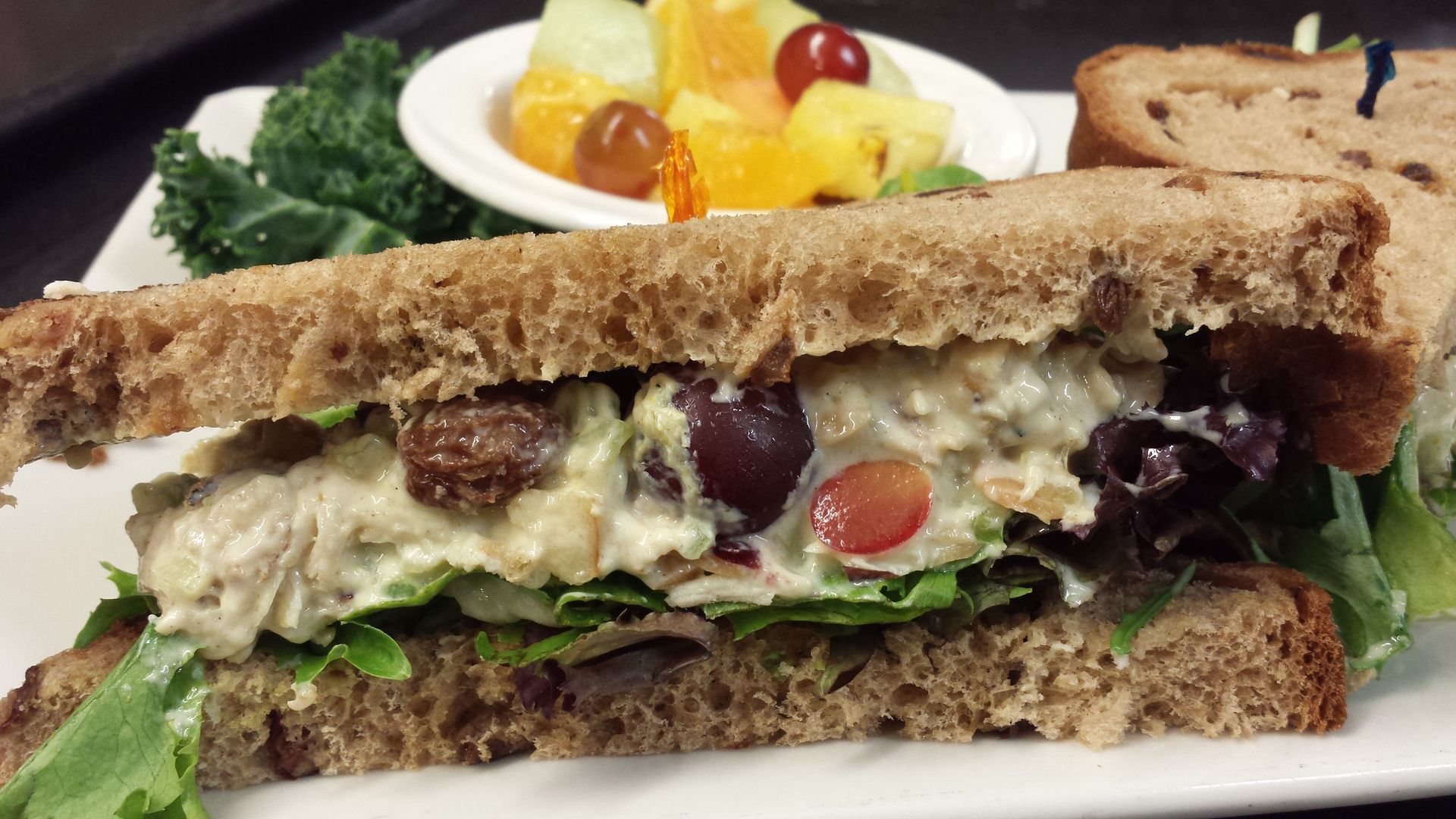 A close up of a sandwich on a plate with a bowl of fruit.