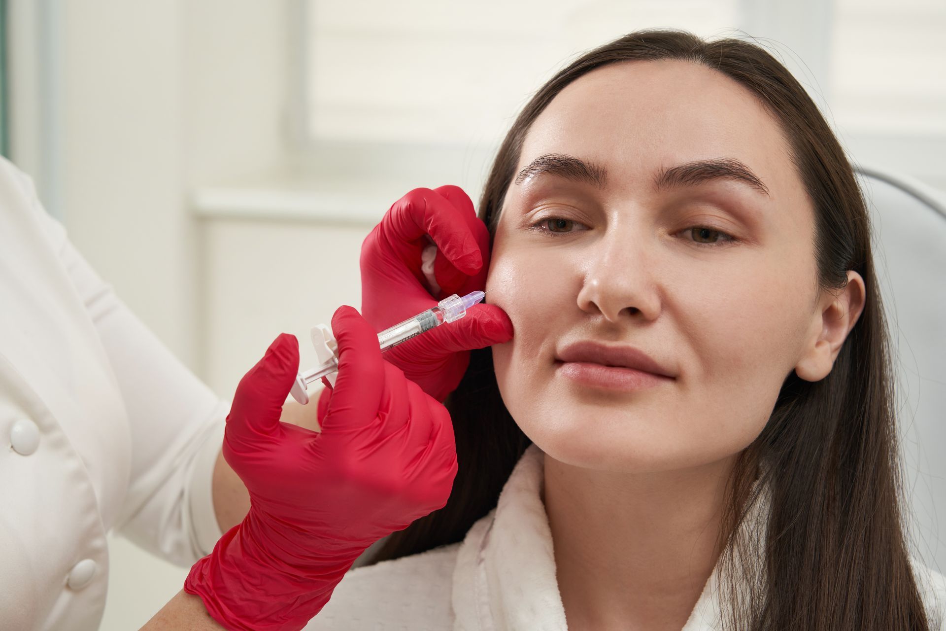 Gloved clinician injecting filler into a woman’s cheek during a cosmetic procedure
