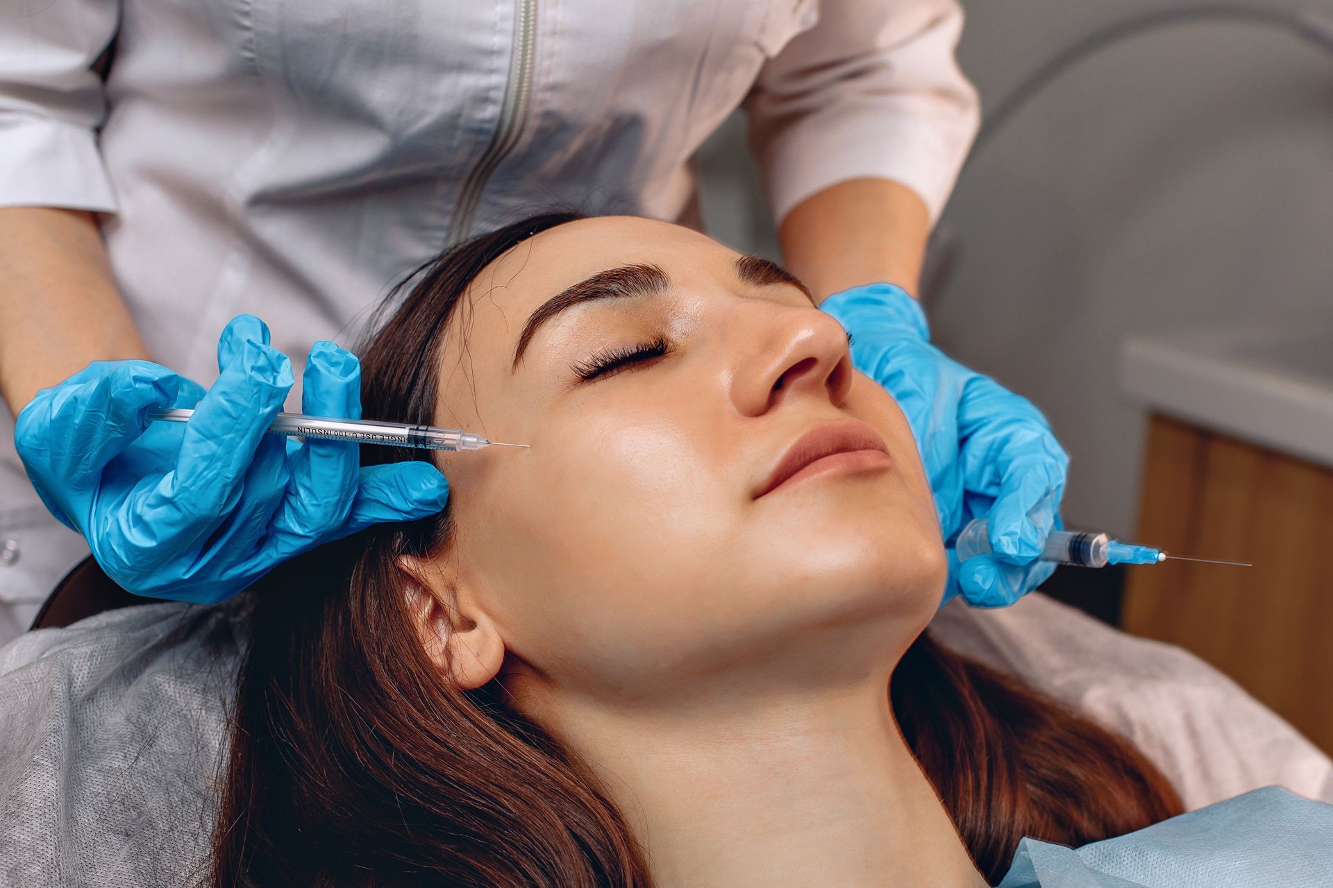 Cosmetic injection being administered to a woman’s forehead in a clinic, with gloved hands
