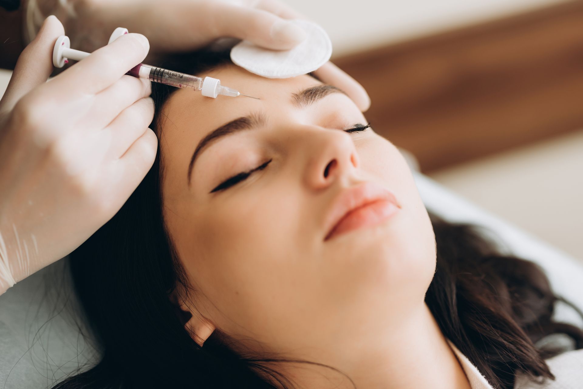 Cosmetic treatment being applied to a woman’s forehead with gloved hands and a syringe