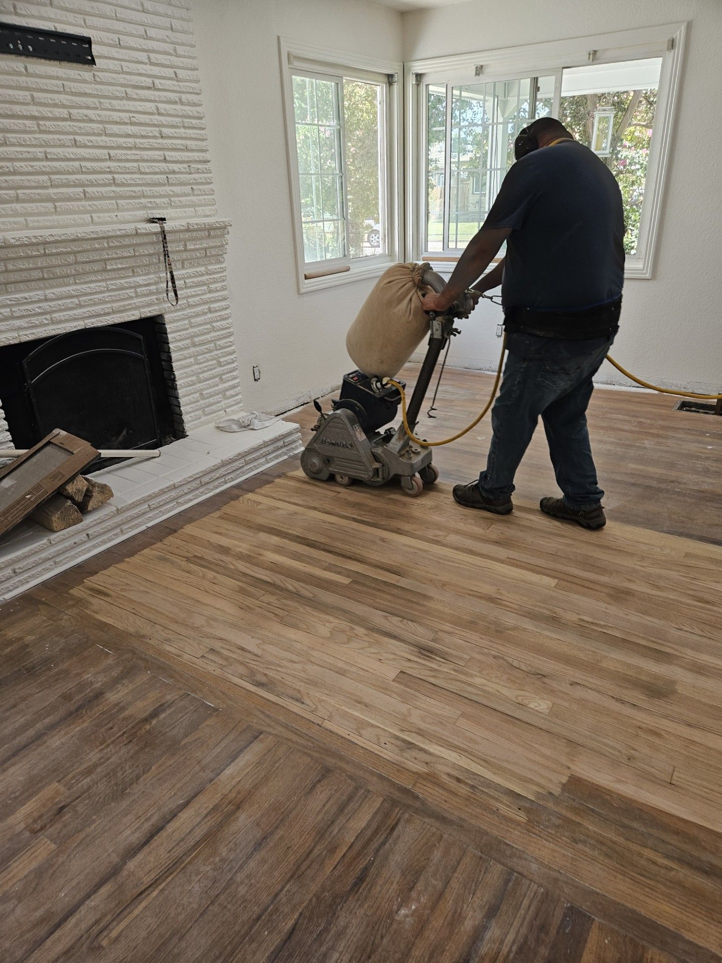 A man is sanding a wooden floor with a machine in a living room.
