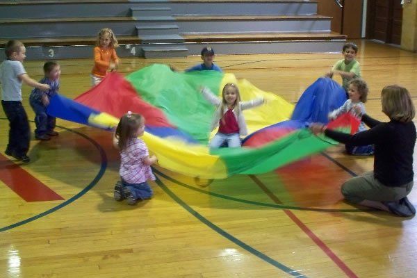 A group of children are playing with parachutes in a gym