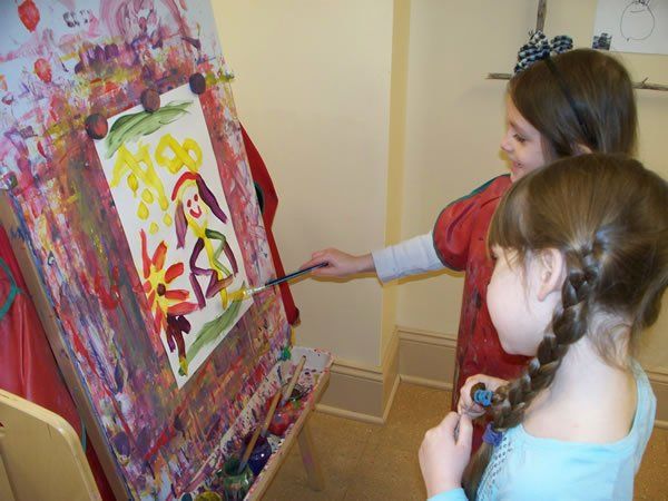 Two young girls are painting on an easel.
