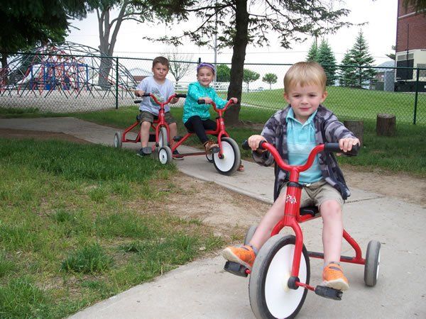 Three children are riding tricycles on a sidewalk