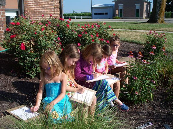 A group of young girls are sitting in the grass looking at papers