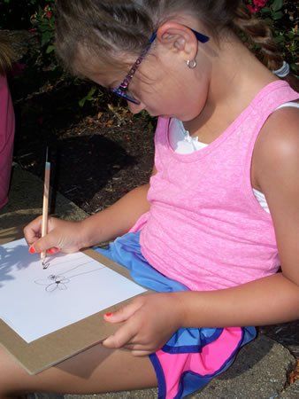 A young girl wearing glasses is drawing a flower on a piece of paper