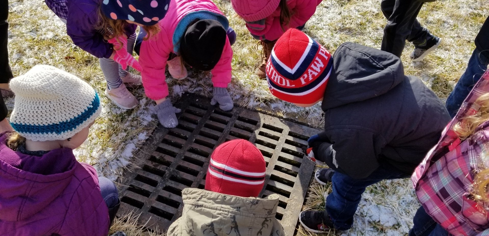 A group of children are looking into a manhole cover.