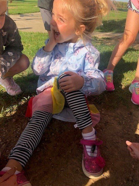 A little girl is sitting on the ground with her mouth open.