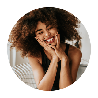 a woman with curly hair is laughing with her hands on her face .