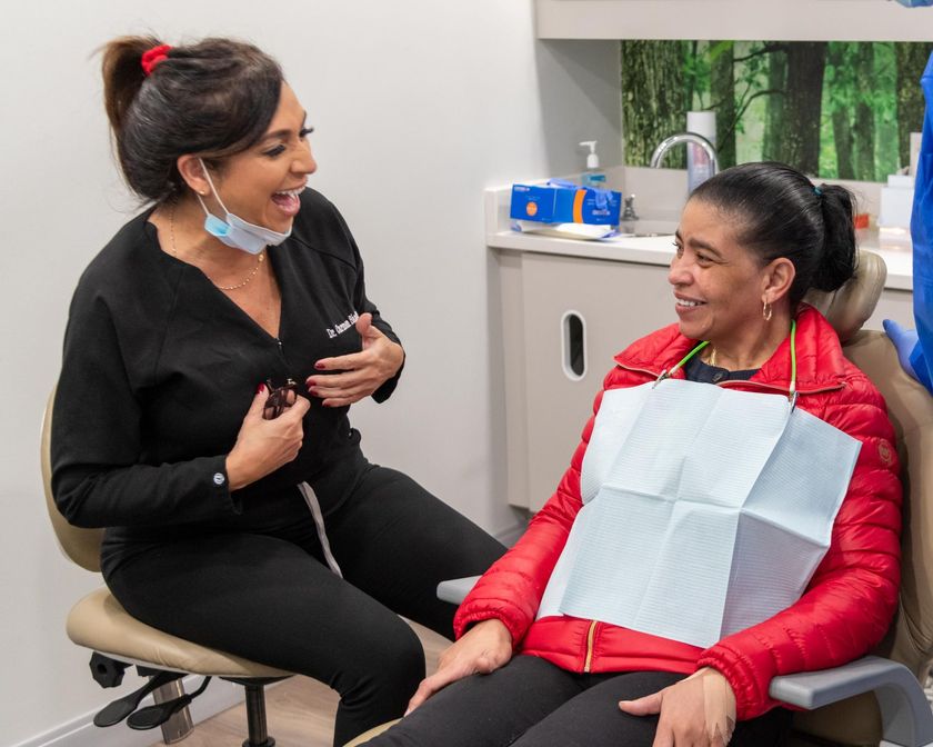 a woman in a red jacket is sitting in a dental chair talking to a dentist .