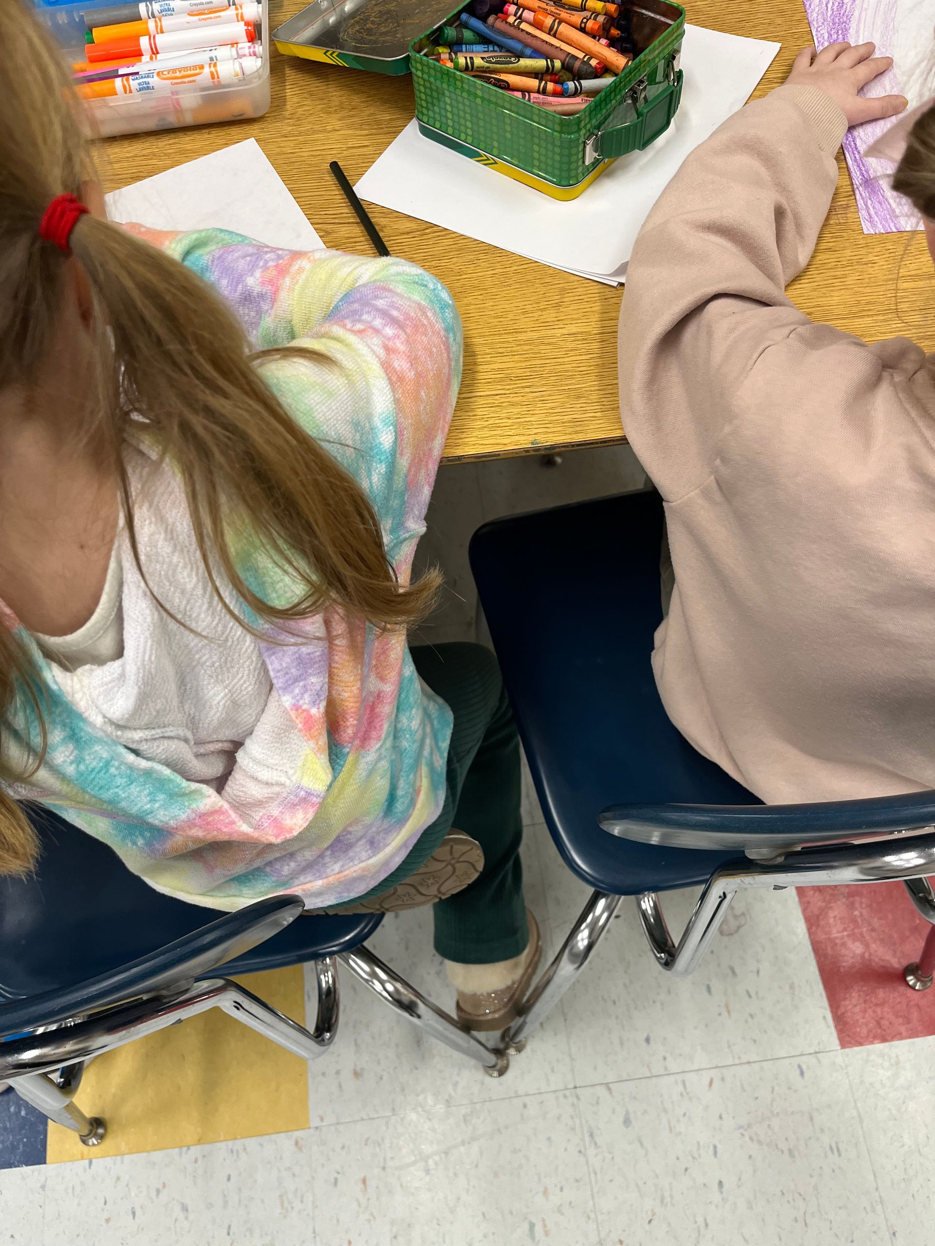 Two young girls are sitting at a table with markers and crayons.