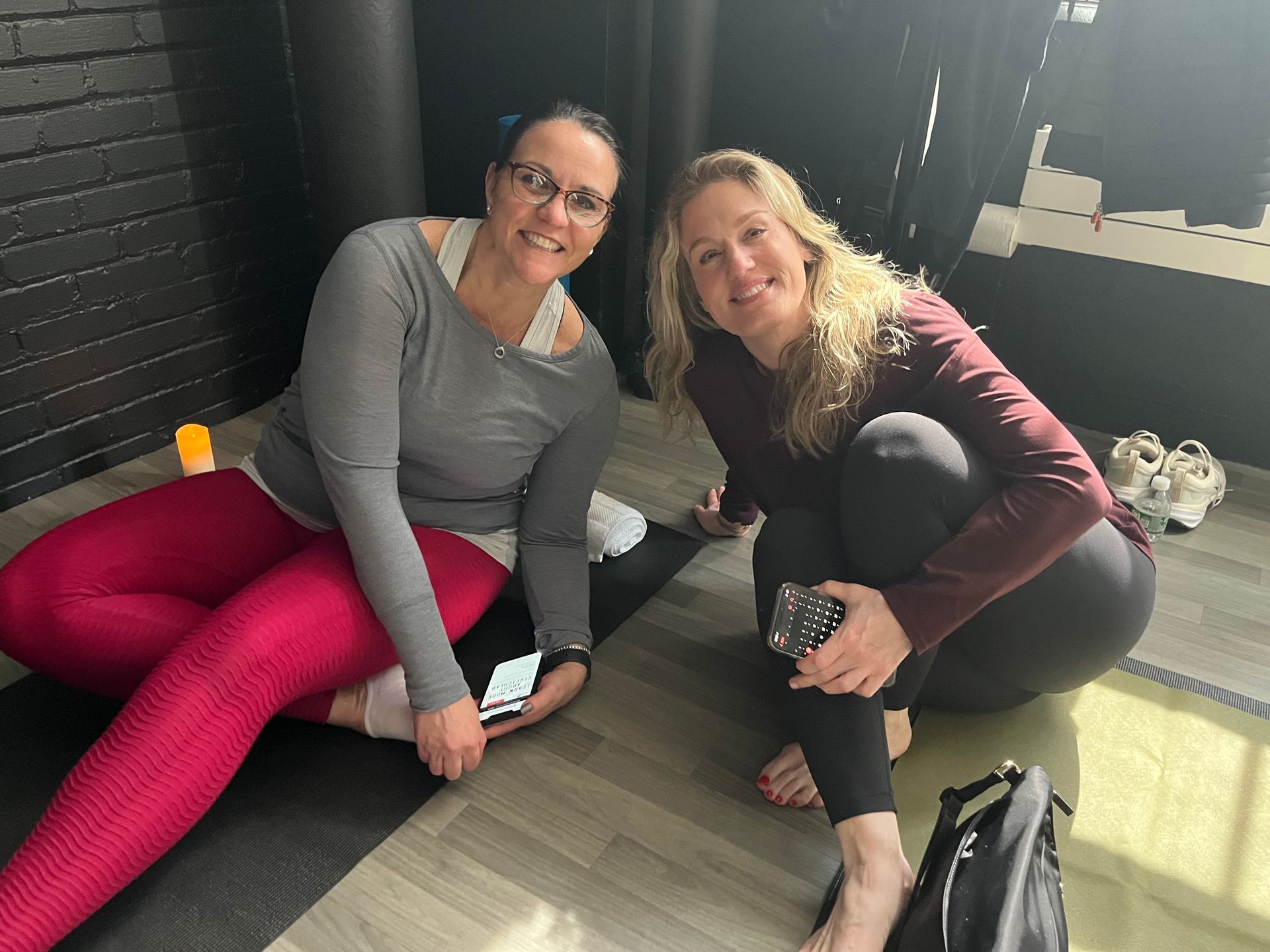 Two women are sitting on a yoga mat on the floor supporting Serenely Guided Foundation for Rare Diseases Fundraiser.