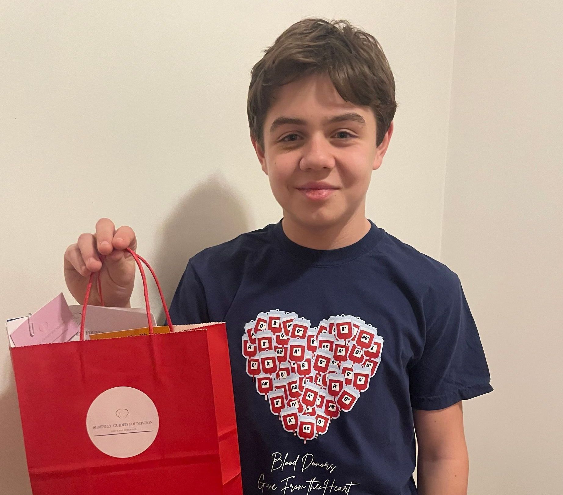 A young boy holding a red bag with a heart on it for Serenely Guided Foundation for Rare Diseases.