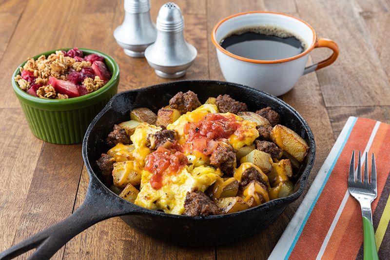 A skillet filled with food and a cup of coffee on a wooden table for Mom's Meals e-gift card