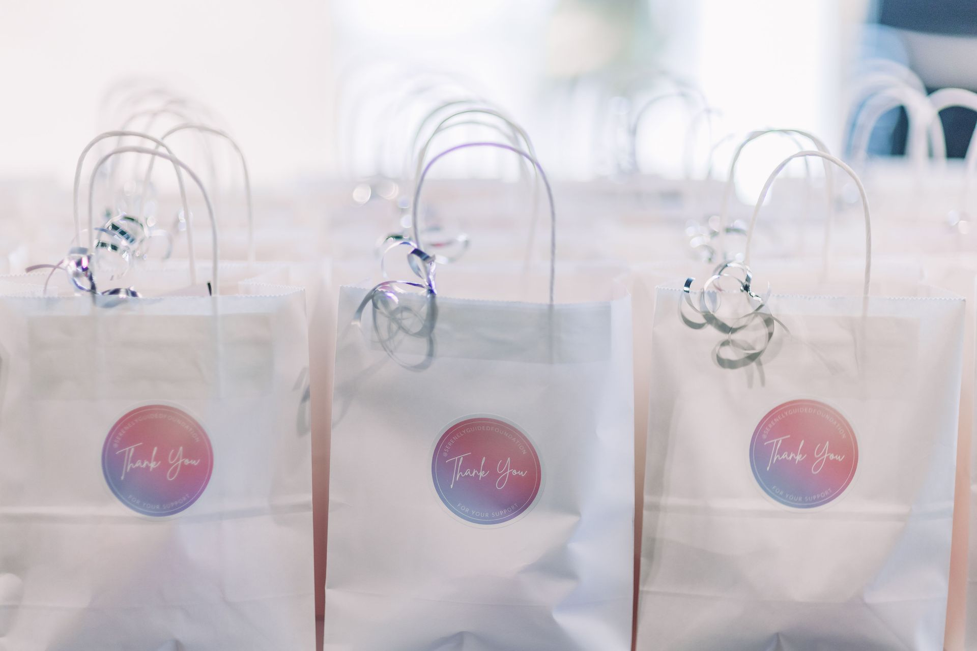 Three white thank you bags with thank you stickers on them are sitting on a table.