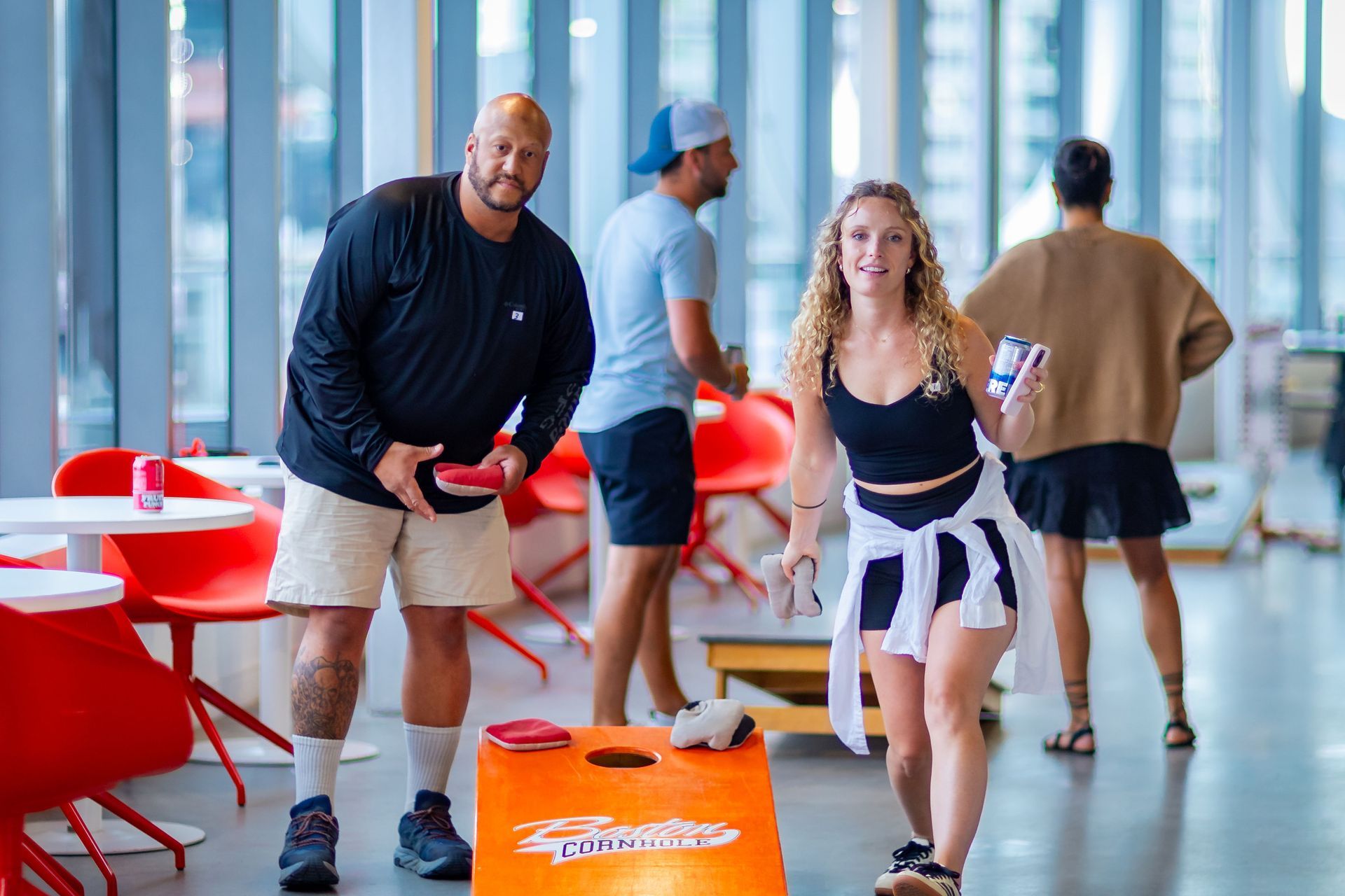 A man and a woman are playing a game of cornhole in a restaurant.