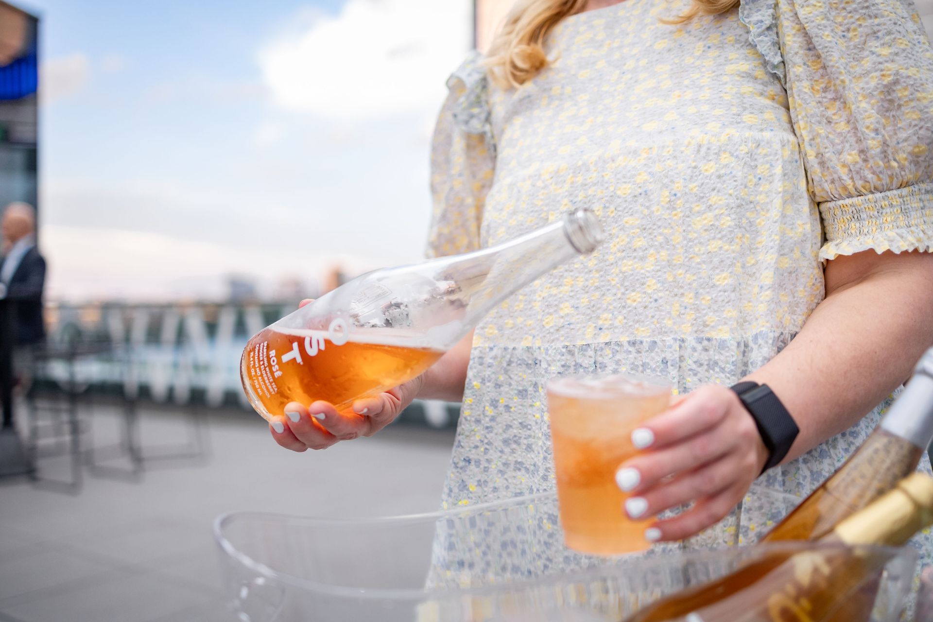 A woman is pouring a drink from a bottle into a glass.