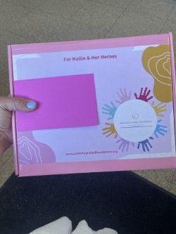 A person is holding a pink box mailing box for patients and caregivers of rare diseases.