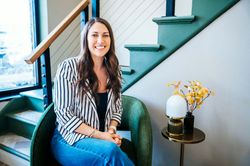 Danielle sitting on teal stairs beside a small table with a lamp and yellow flowers, smiling at the camera