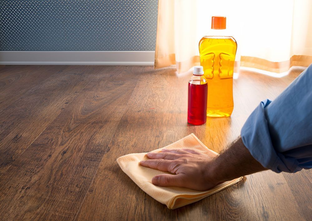 A Person Is Cleaning A Wooden Floor With A Cloth — Kyall Chalker Floor Sanding & Polishing In Taree, NSW