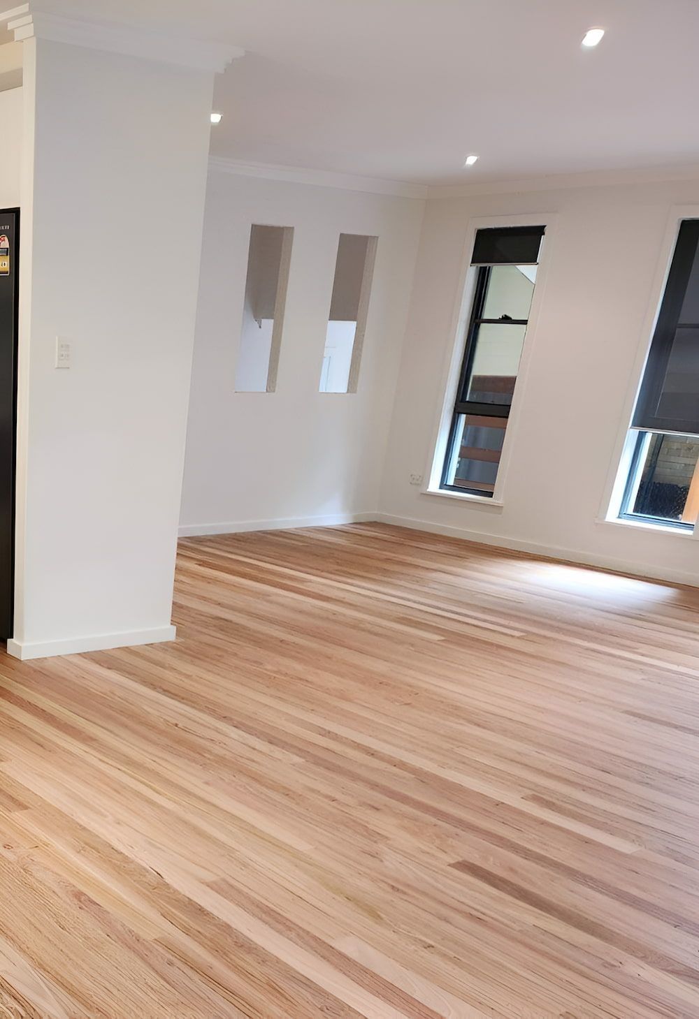 An Empty Living Room With Hardwood Floors And White Walls — Kyall Chalker Floor Sanding & Polishing In Taree, NSW