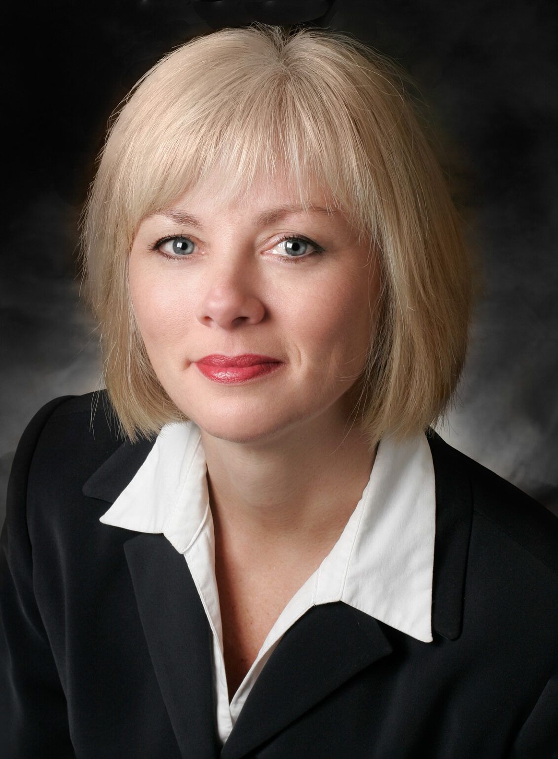 a woman with blonde hair and blue eyes is wearing a black jacket and white shirt
