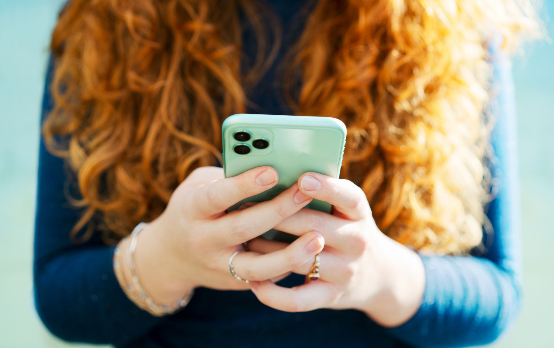 A woman with red hair is holding a cell phone in her hands.