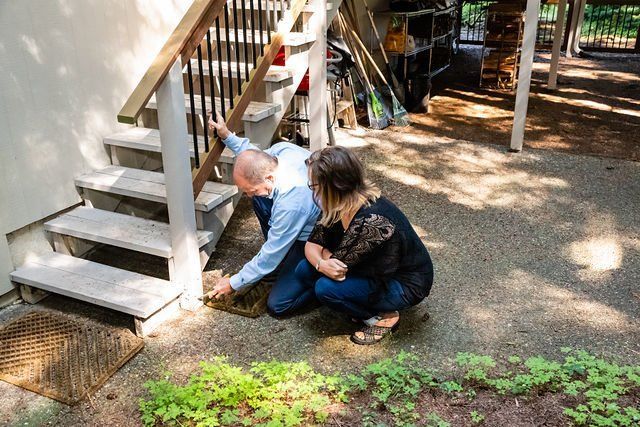 Mitch and a woman are kneeling down next to a set of stairs.