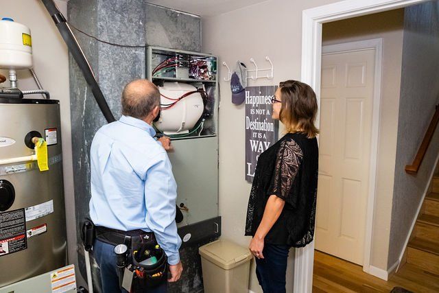 Mitch and a woman are looking at an air conditioner in a room.