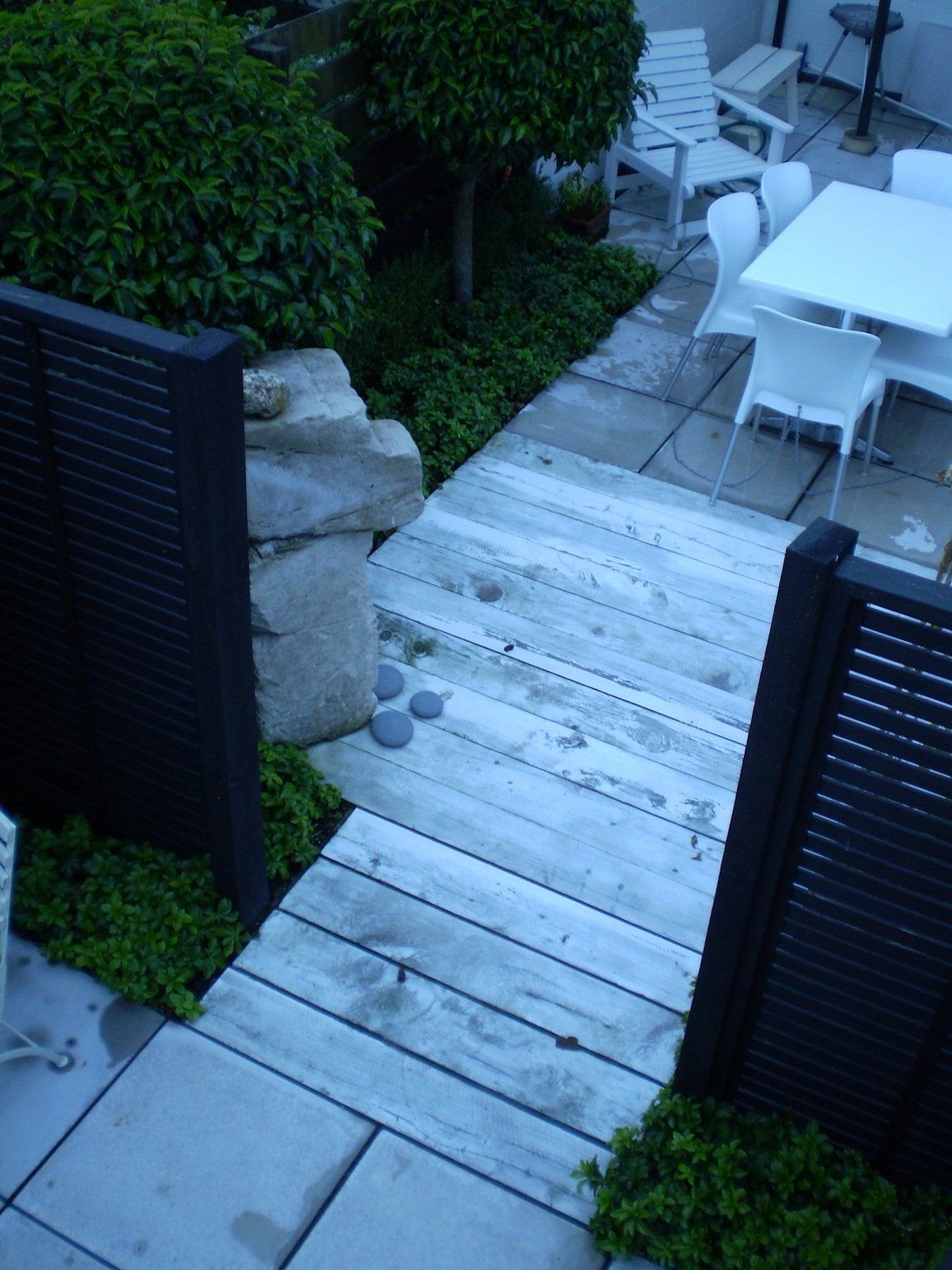 A wooden walkway leads to a patio with a table and chairs