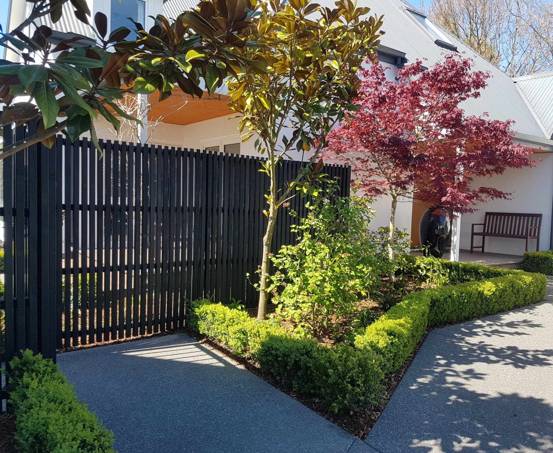 A black fence surrounds a lush green garden in front of a house