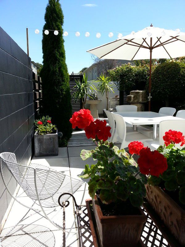 A patio with red flowers and a white umbrella