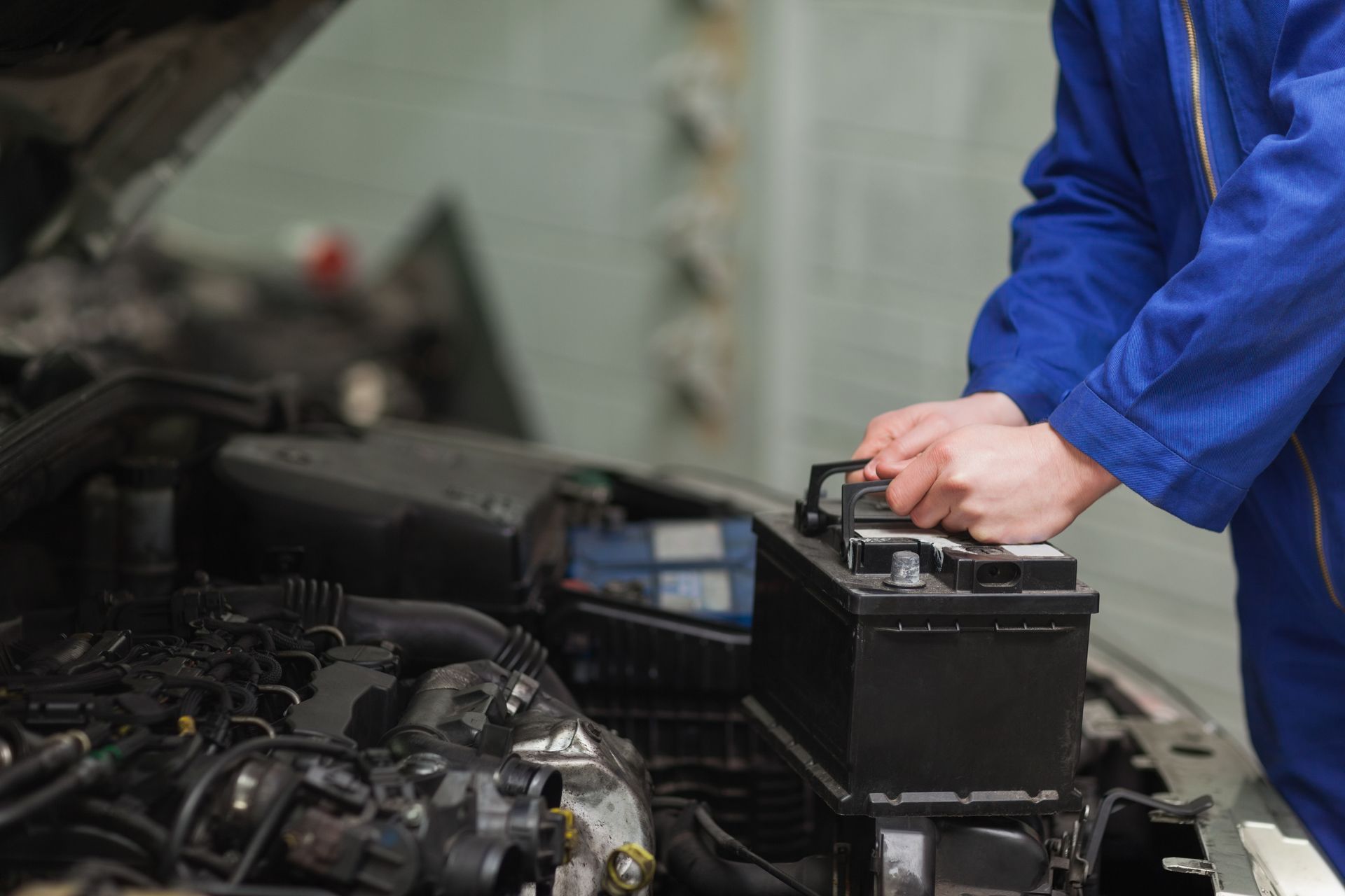 A mechanic is working on a car battery in a garage.