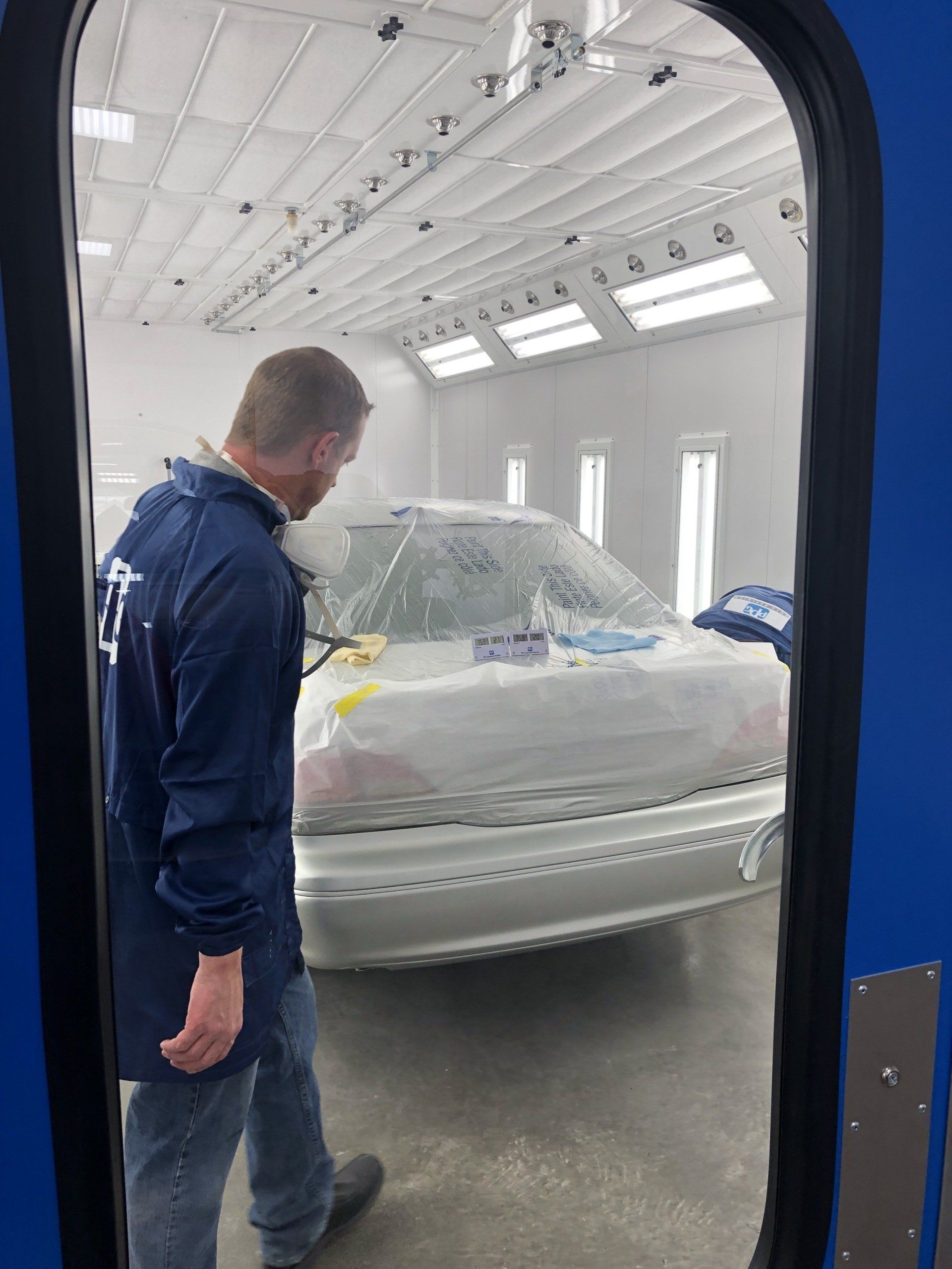 A man is standing in front of a car in a paint booth.
