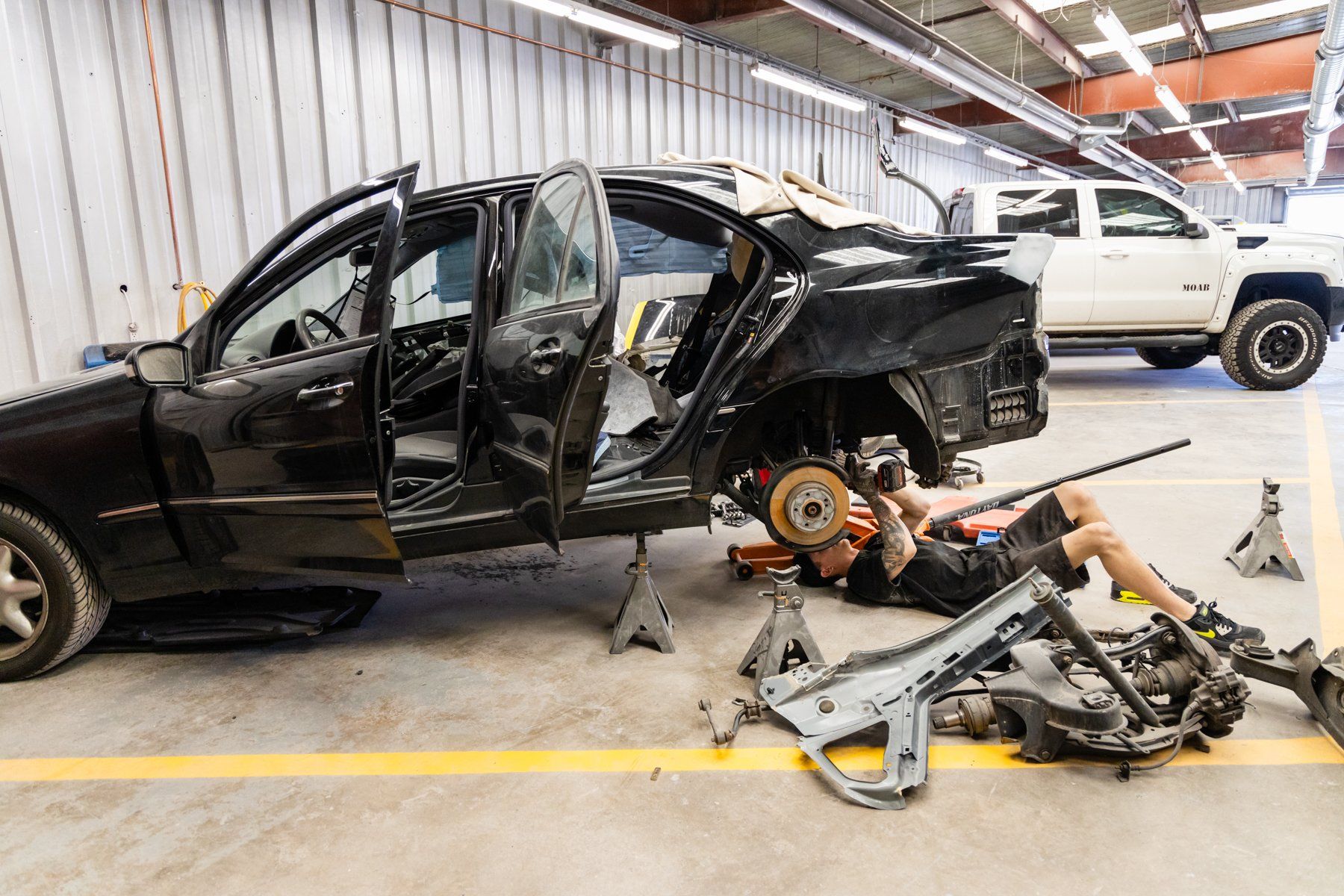 A man is laying on the ground working on a car in a garage.