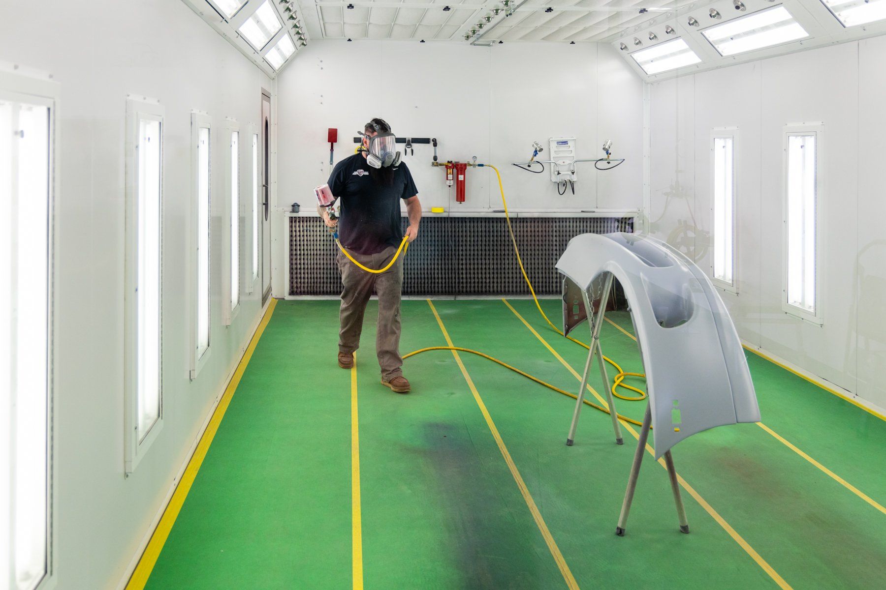 A man is spraying a car bumper in a paint booth.