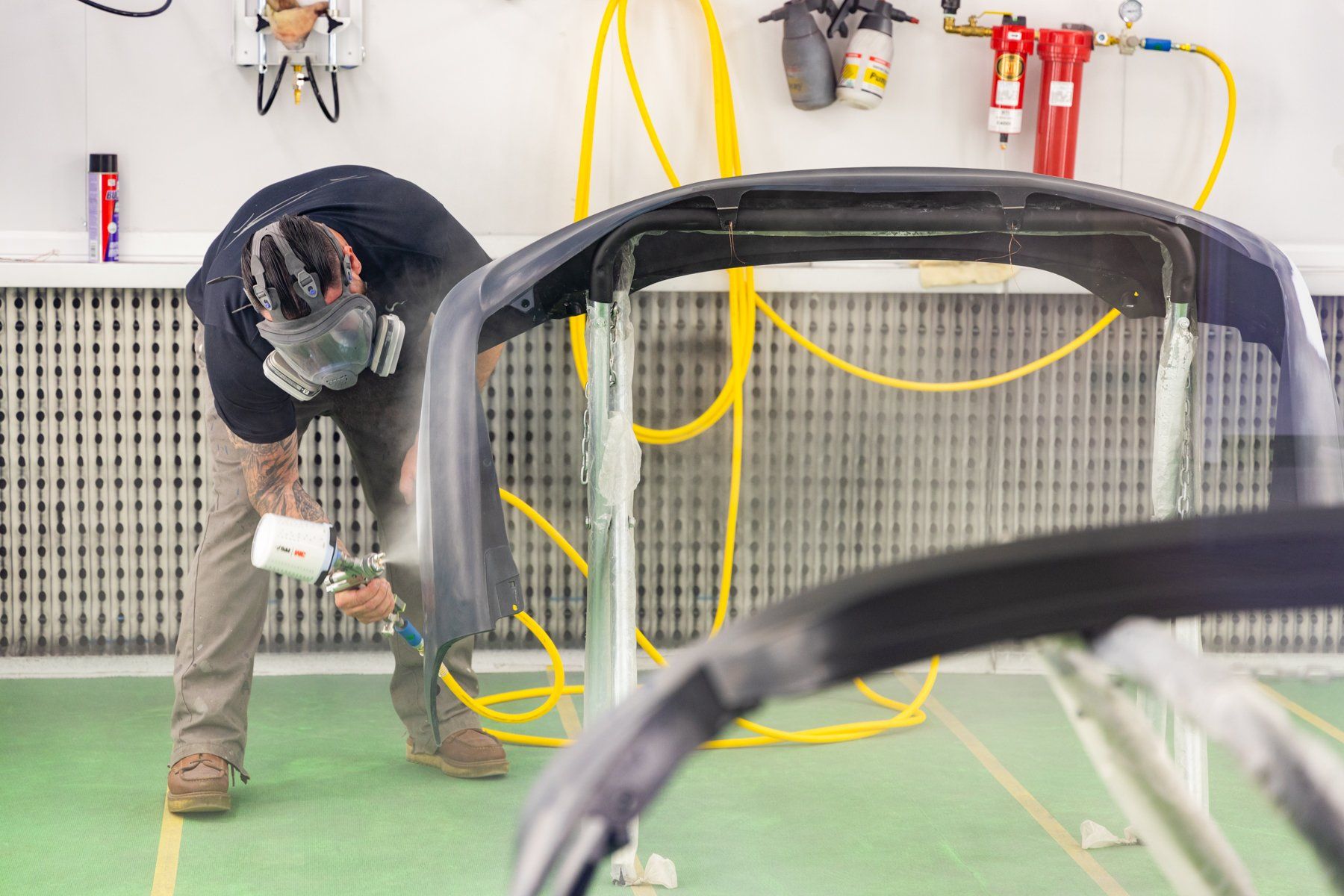 A man is spray painting a car bumper in a paint booth.