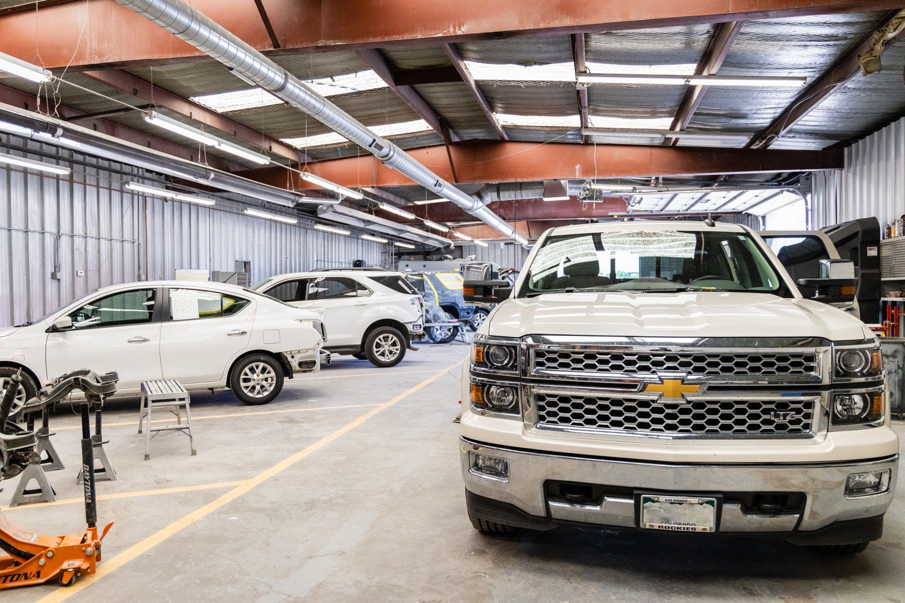 A white truck is parked in a garage next to a row of cars.