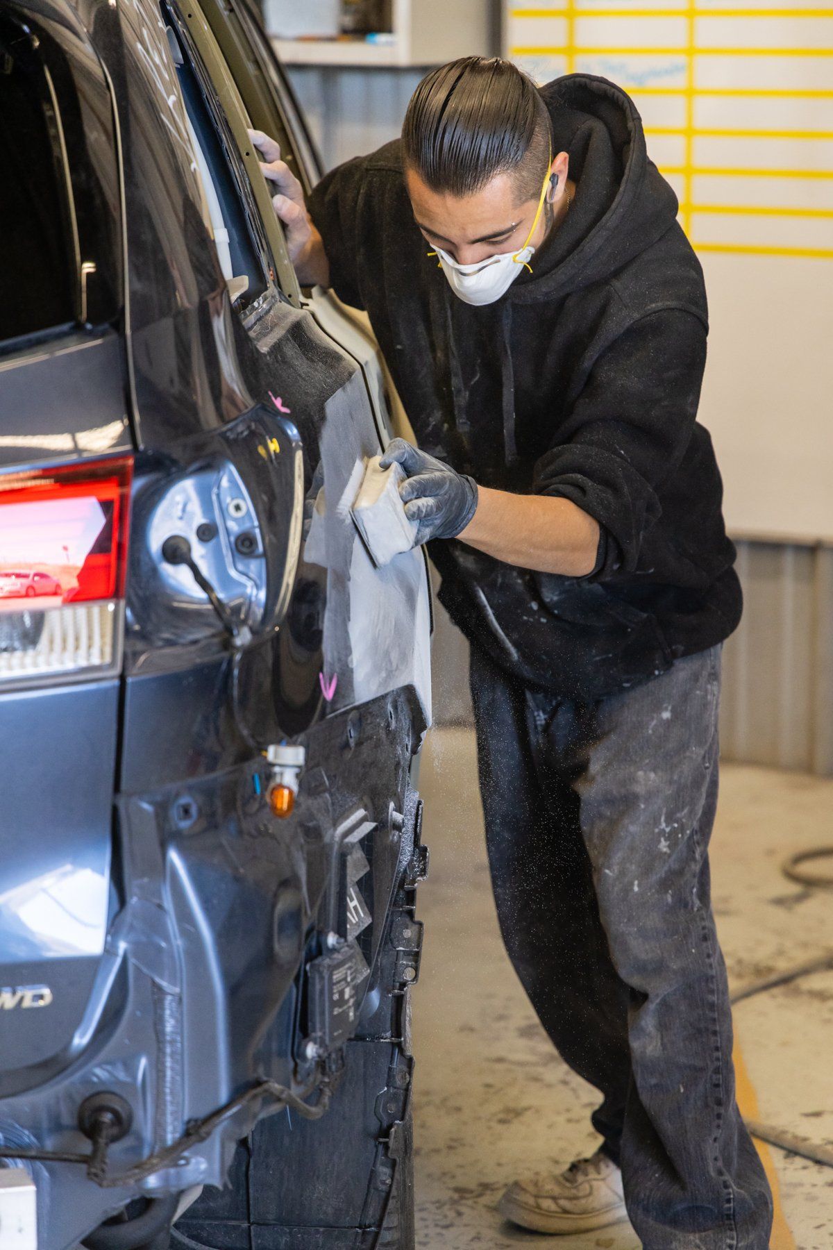 A man wearing a mask is working on a car in a garage.