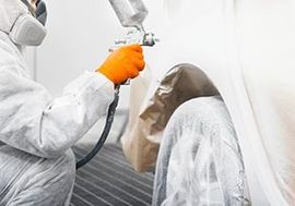 a man in a protective suit is spray painting a car .